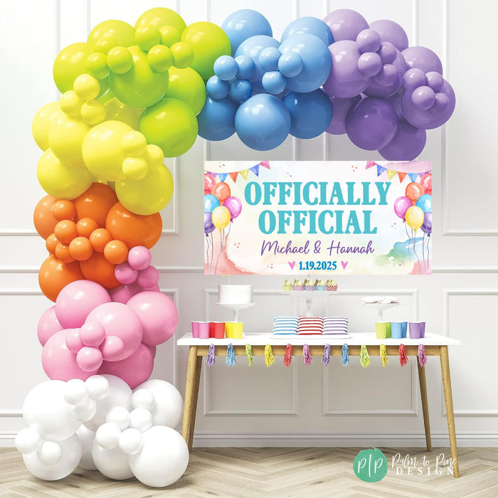 a colorful balloon arch and a table with party decorations, including a banner that reads " Officially Official Michael & Hannah".