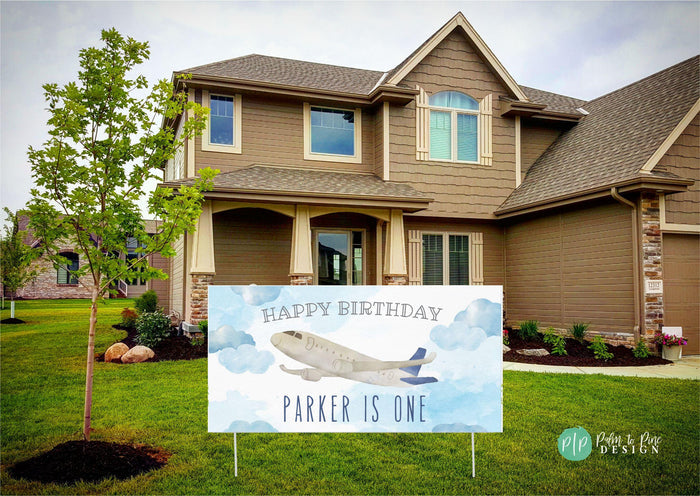 A blue and white birthday sign with an airplane flying through clouds. The sign reads 'Happy Birthday Parker is One'