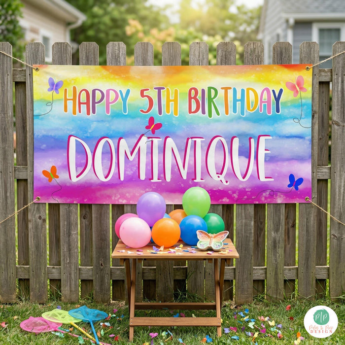 Rainbow butterfly birthday party setup with personalized banner and vibrant themed decor in backyard