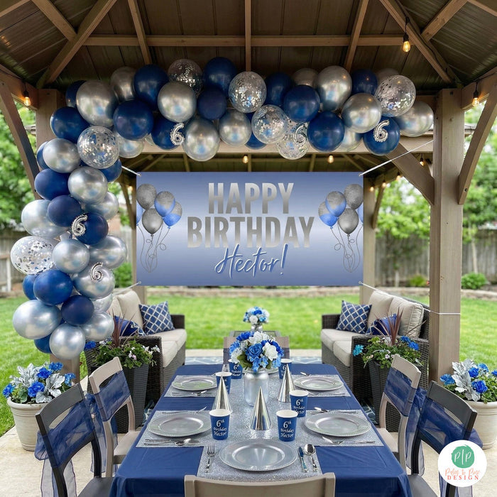 Navy and silver birthday party set up outdoors under covered patio with personalized banner and balloon garland, and table setting in navy and silver color scheme