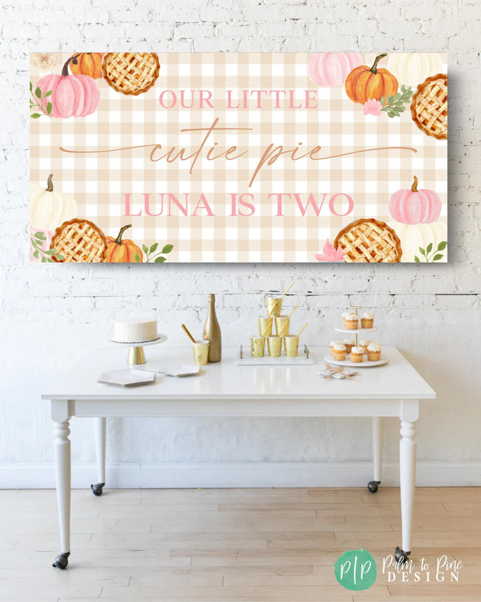 pink cutie pie birthday banner with fall pumpkins and lattice crust pies on gingham background in front of desser table
