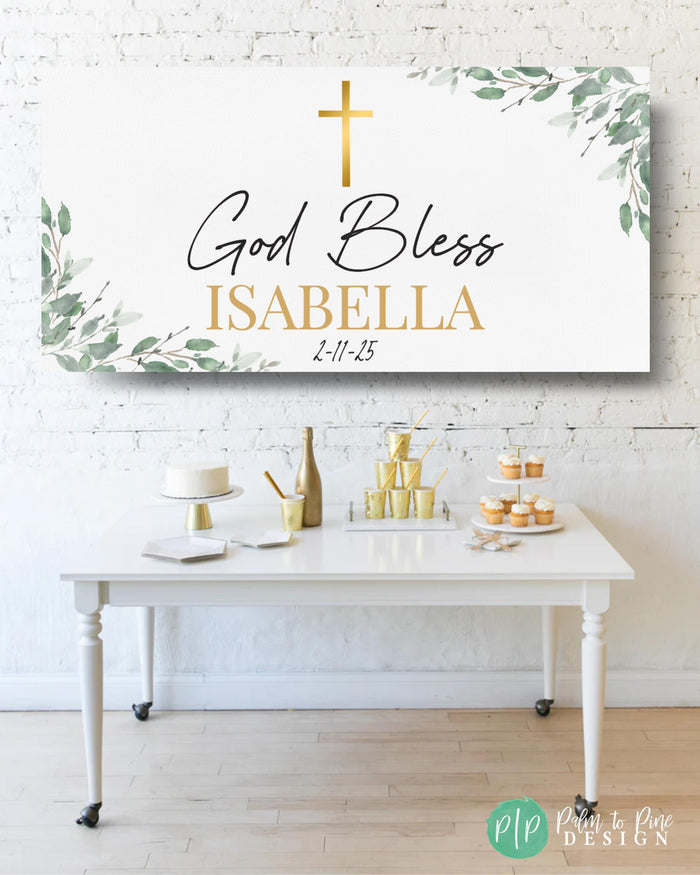 A baptism celebration featuring a personalized banner that reads God Bless with name and baptism date hung above a simple white table with a cake, cupcakes, and other desserts
