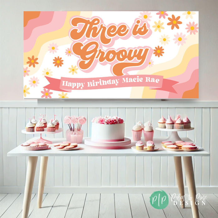 Three is Groovy Retro birthday banner for girls party in front of a simplistic dessert table
