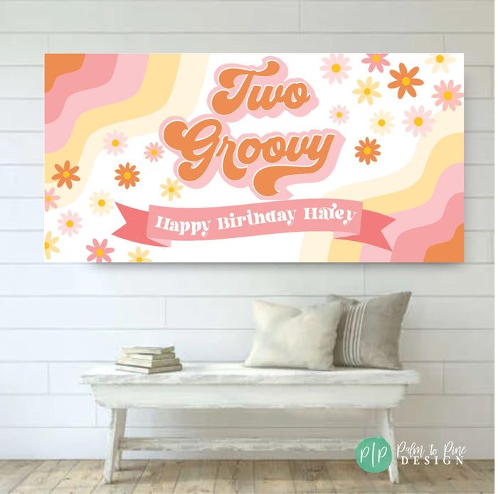 A white banner with a pink and orange wavy design. The banner has the text 'Two Groovy' in orange with a pink outline. The banner also has the text 'Happy Birthday Hailey' in pink with a white outline. The banner is decorated with white and yellow flowers.