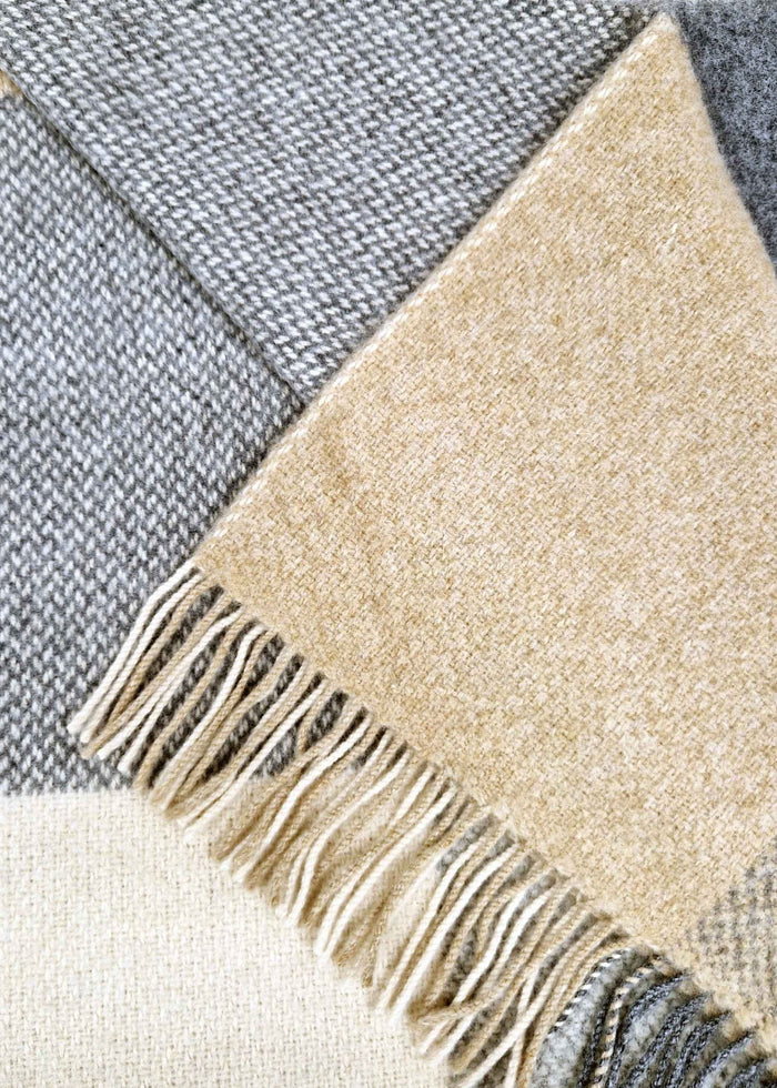 Close-up of a checkered blanket with beige and gray colors and fringed edge.