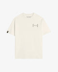 A front view of Le T-Shirt in cream, laid flat on a white background. The image highlights the high ribbed collar, oversized fit, the black mirror c'est normal logo on the chest, and the black satin cuff tag on the sleeve.