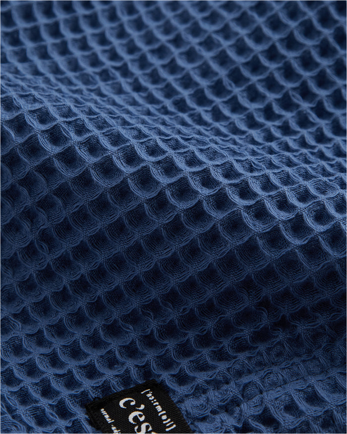 Le Waffle Shorts in azure — macro view of the textured waffle fabric and C'est normal tag