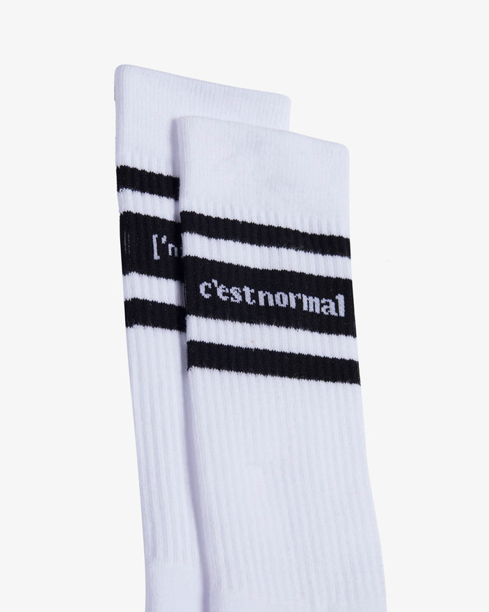 A close-up shot of two pairs of Les Socks in white, highlighting the ribbed texture and the black stripes with the c'est normal logo in white contrast stitching.