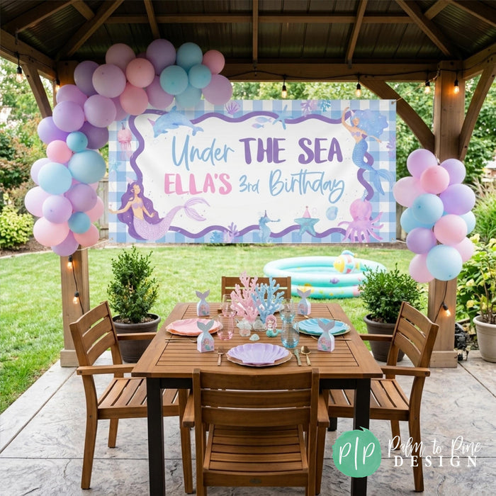 Under the sea birthday banner with mermaid theme hanging above an outdoor party table setup