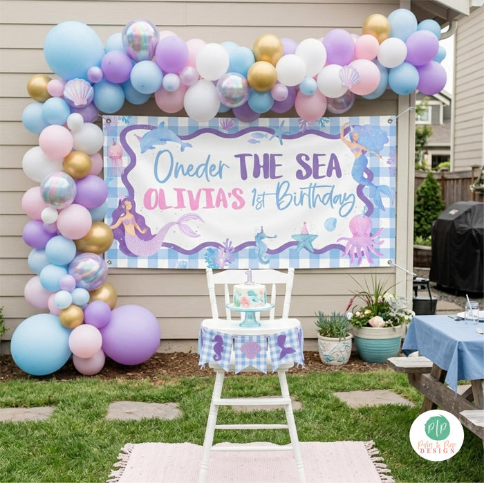 Mermaid Oneder the sea banner with pastel balloon garland for an outdoor first birthday cake smash photoshoot
