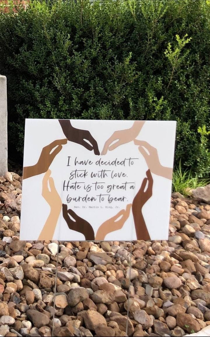 a social justice yard sign with a message about love and unity, surrounded by a group of hands of different skin tones forming a circle.