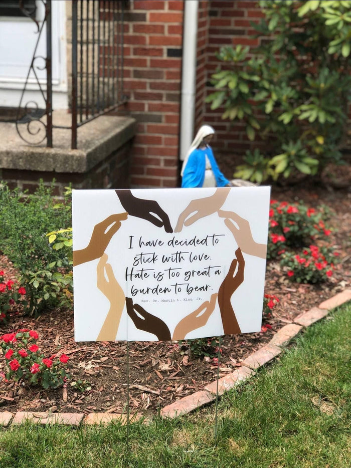 A social justice yard sign with a Martin Luther King Jr. quote about love and unity, featuring a graphic of hands of different skin tones forming a heart shape.