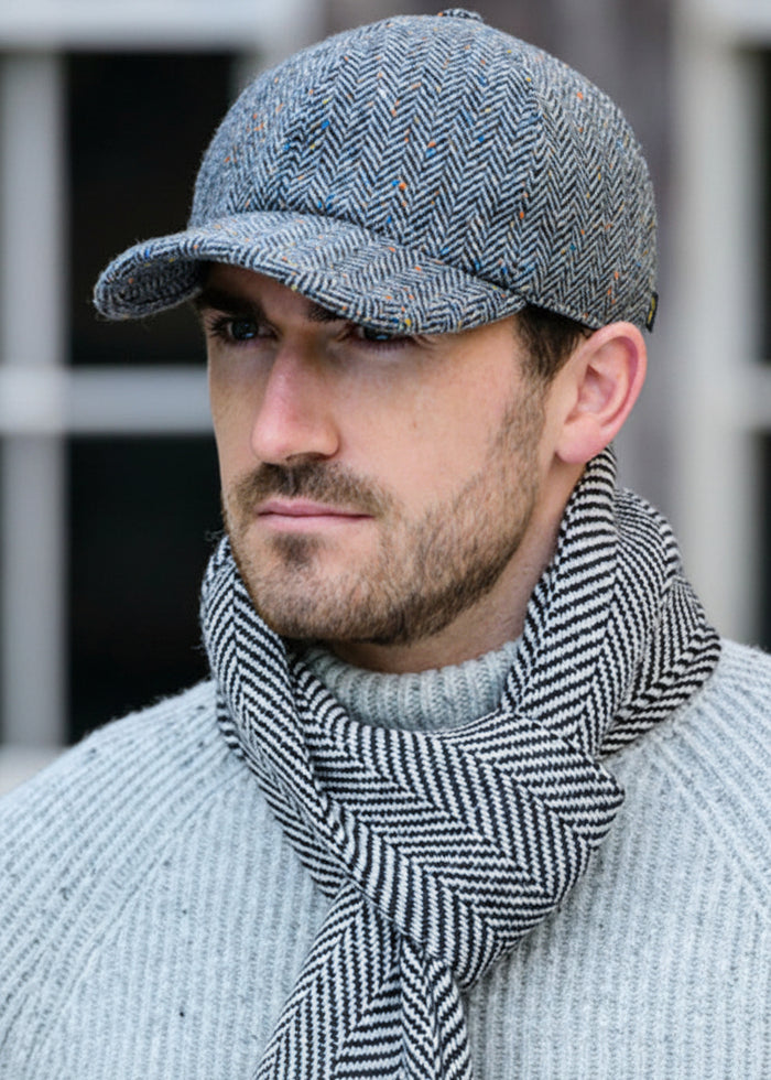 Man wearing a gray herringbone cap and scarf against a blurred background