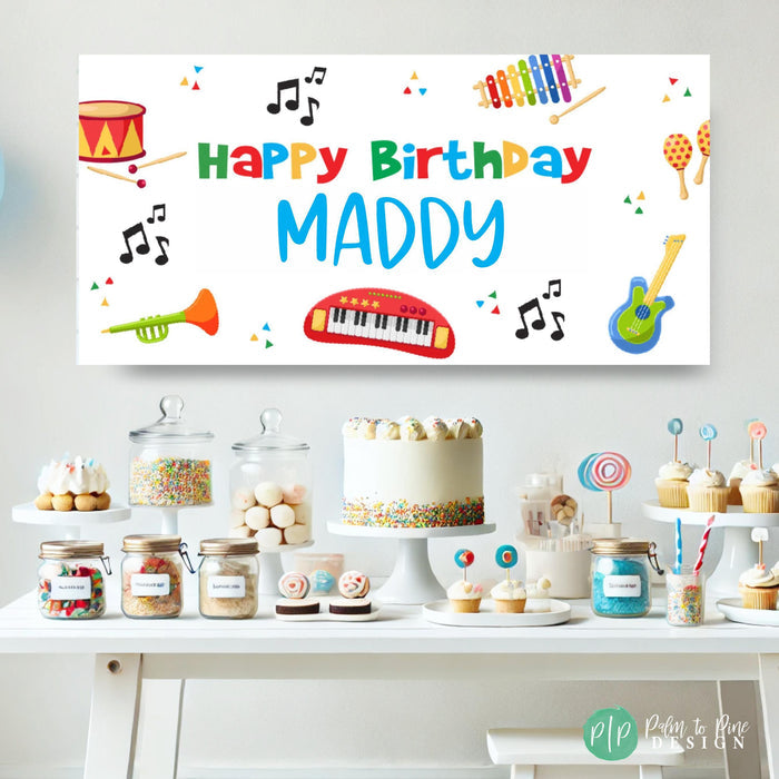 Rainbow-colored birthday banner for kids with musical designs, including instruments and notes on a white background in front of a dessert table