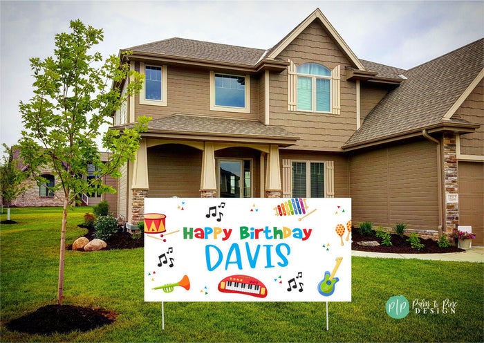 Kids' birthday party decoration: musical banner with rainbow colors, instruments, and notes on a white background in front yard of house