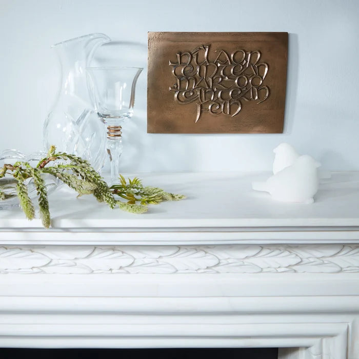 Decorative wooden plaque with engraved text on a white surface with glass pitcher and candle.