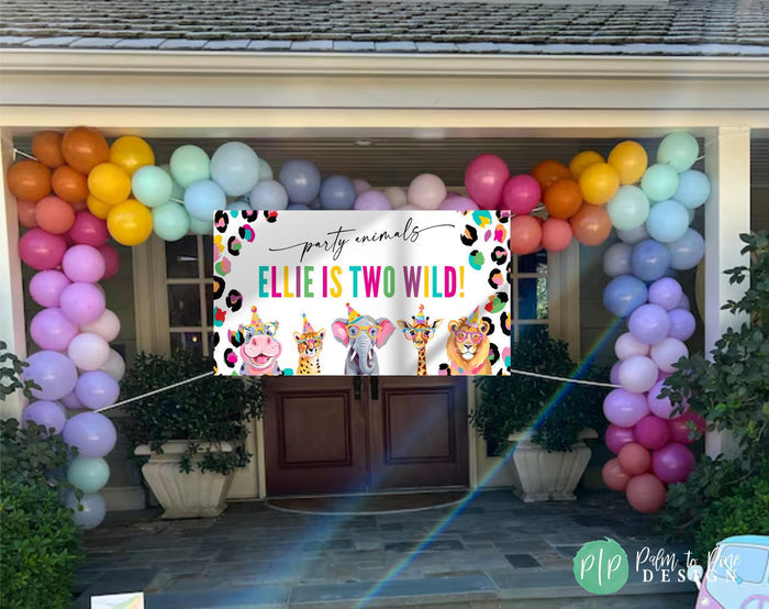 Bright rainbow cheetah print jungle banner with hippo, elephant, lion, cheetah, and giraffe in party hats hung outside house with colorful balloon garland