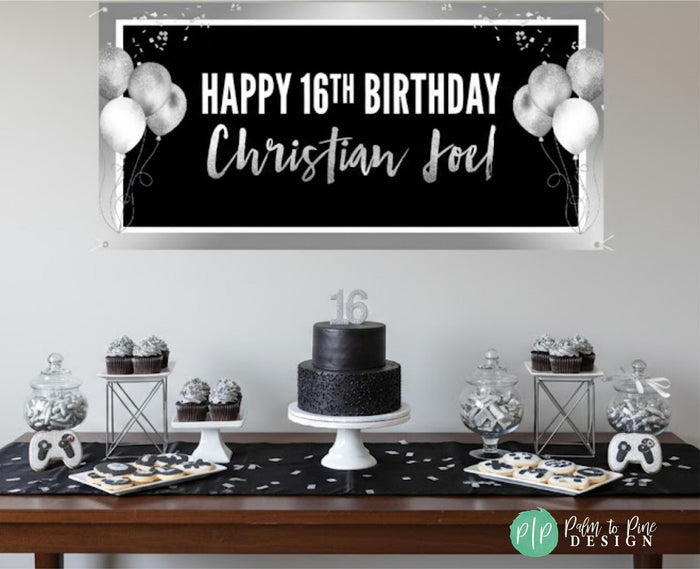 a birthday celebration setup with a black and silver theme. The centerpiece is a large banner that reads "Happy 16th Birthday Christian Joel!" The banner is surrounded by white balloons, and there is a black and white birthday cake on a table. The table also has various desserts, including cupcakes and cookies.