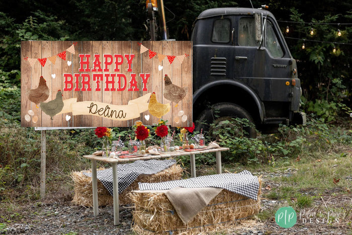 A wooden sign with a "Happy Birthday" message and illustrations of chickens is displayed in front of a rustic truck and hay bales, suggesting a birthday celebration in a rural setting.