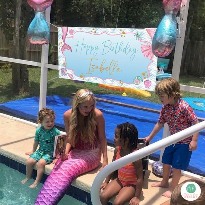 Kids pool party with mermaid sitting on the edge of the pool, and hung behind them is a birthday banner that reads Happy Birthday with child's name