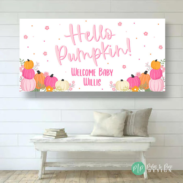 Pink and orange autumn-themed baby shower banner. The banner features the text 'Hello Pumpkin! Welcome Baby Willis.'  Pumpkins in varying shades of pink, orange, and white are arranged along the bottom. Small pink flowers and gold dots are scattered across the white background.