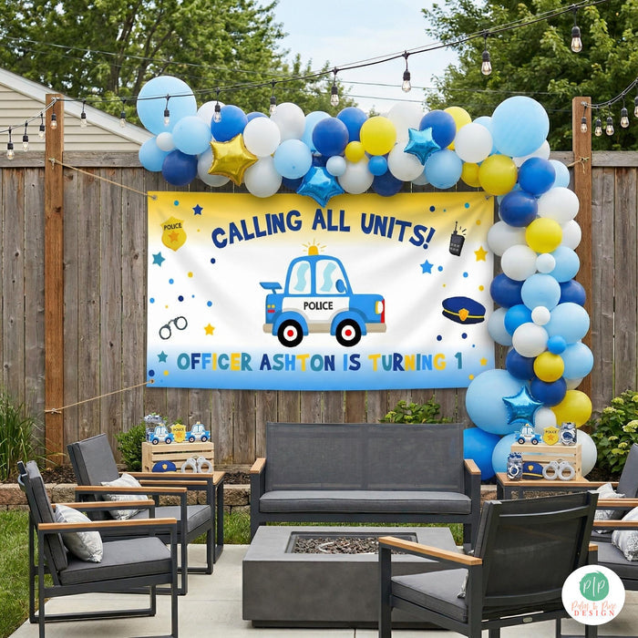cute police car themed birthday party in backyard with personalized banner hung on a fence and surrounded by a blue and yellow balloon garland