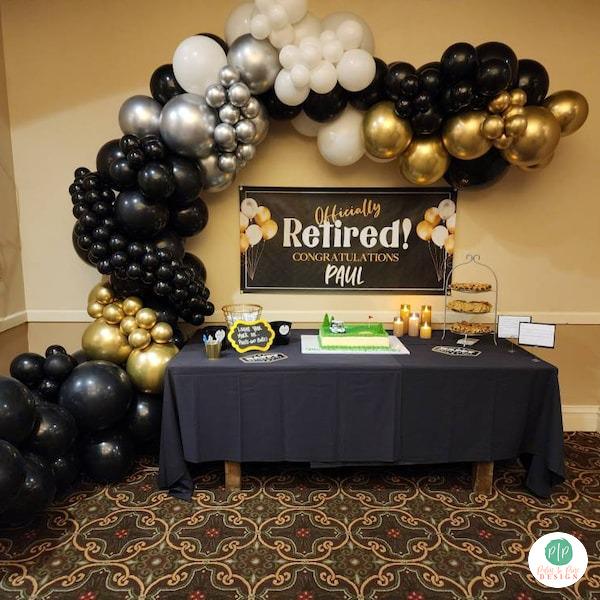 a table decorated with black and gold balloons, a banner that reads " Officially Retired! Congratulations Paul", and a cake on the table.