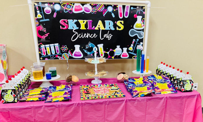 girls science birthday theme party in front of science themed dessert table with pink tablecloth