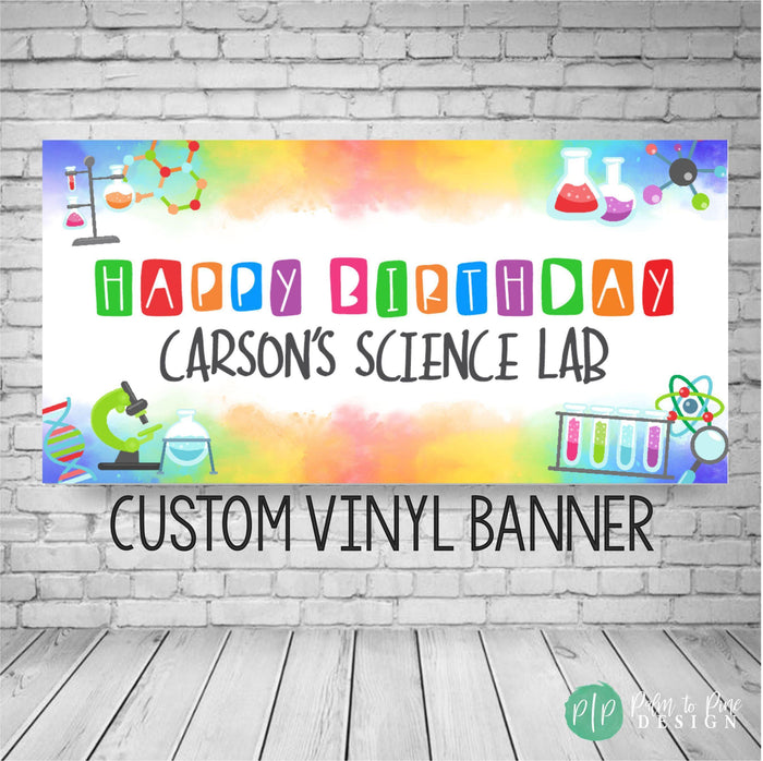 A colorful science-themed birthday banner with the text 'Happy Birthday Carson's Science Lab' and the words 'Custom Vinyl Banner' at the bottom. The banner has a watercolor background with a variety of science-related images, including beakers, test tubes, molecules, and a microscope.