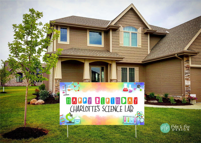 A colorful birthday yard sign with a science theme. The sign has a white background with a rainbow watercolor effect. The text on the sign reads 'Happy Birthday Charlotte's Science Lab'. The sign is decorated with images of beakers, test tubes, microscopes, and other science-related items.