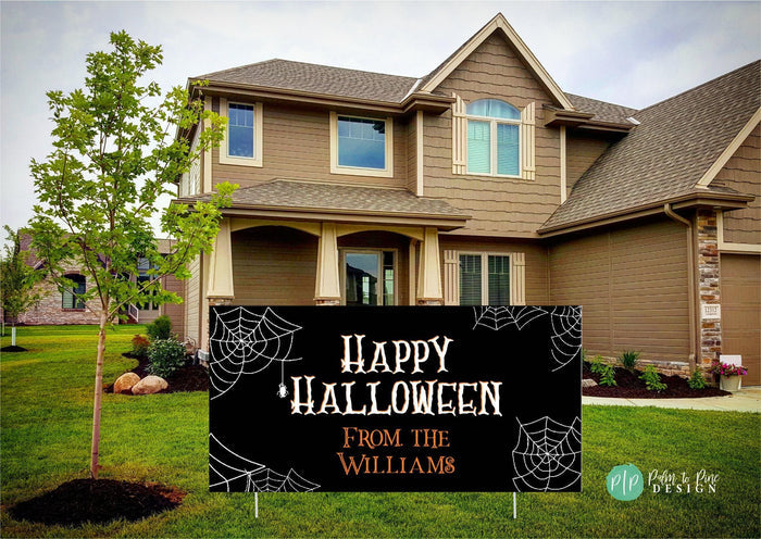 A two-story house with a porch, surrounded by a well-maintained lawn and landscaping. In front of the house, there is a Halloween-themed sign that reads "Happy Halloween From the Williams".