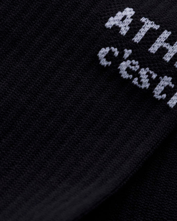 A close-up shot of the black ribbed fabric of The Athlétique Socks, highlighting the white contrast stitching of the c'est normal logo.