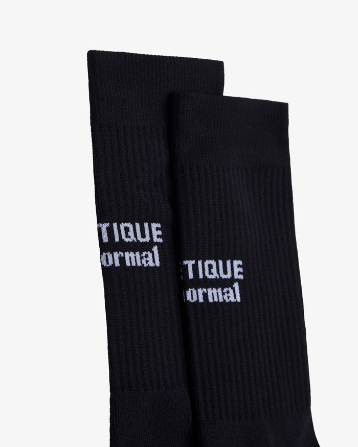 A close-up shot of two black The Athlétique Socks laid flat on a white background, highlighting the white c'est normal logo in contrast stitching at the mid-calf.