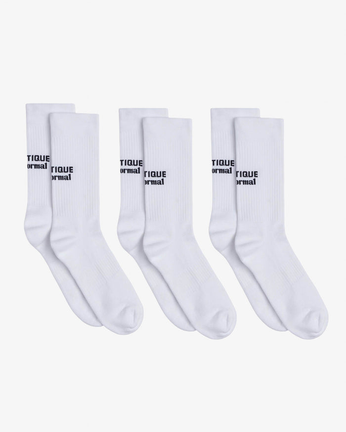 Three pairs of The Athlétique Socks in white, laid flat on a white background. The image highlights the black contrast stitching of the c'est normal and Athlétique logos at mid-calf.