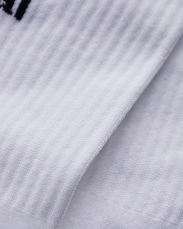 A close-up shot of the white ribbed fabric of The Athlétique Socks, highlighting its texture and a small part of the black embroidered c'est normal logo.