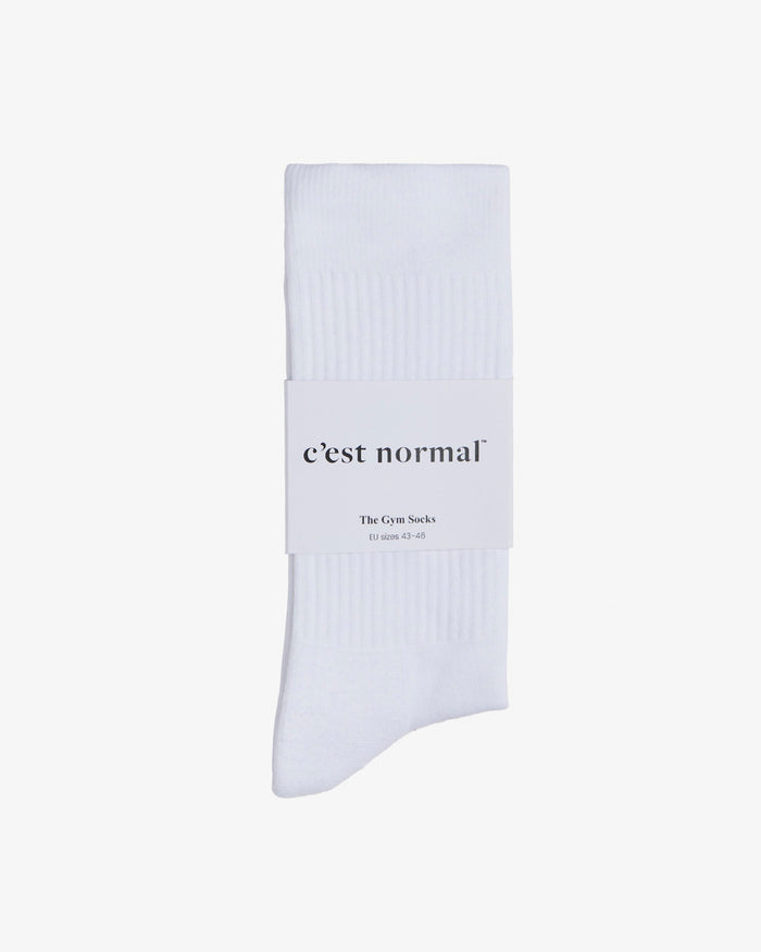 A pair of white The Athlétique Socks wrapped in a c'est normal branded paper sleeve, laid flat on a white background. The ribbed texture of the cotton socks is visible.
