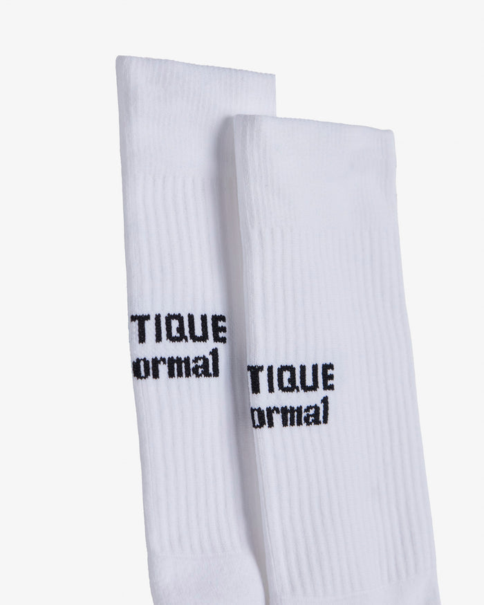 A close-up shot of two white The Athlétique Socks, highlighting the ribbed texture and the black c'est normal logo in contrast stitching at the mid-calf.