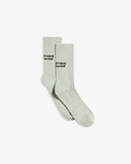 A pair of The Athlétique Socks in sage green, laid flat and slightly overlapping on a white background. The image highlights the ribbed cuffs and the black embroidered c'est normal logo at mid-calf.