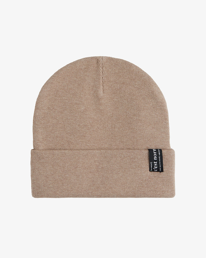 The Beanie in beige laid flat against a white background, featuring a soft fine knit, a fold-over cuff, and the signature black c'est normal label on the right side.