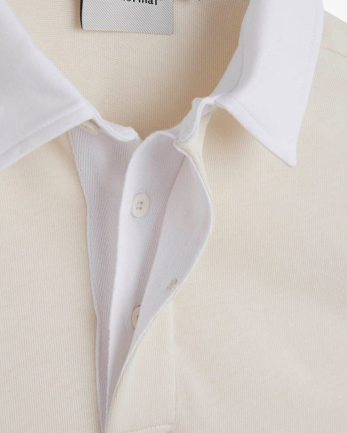 A close-up shot of the white collar and covered placket of The c'est pari Rugby Shirt in Cream. The image highlights the details of the buttons and the interior label featuring the c'est normal logo.