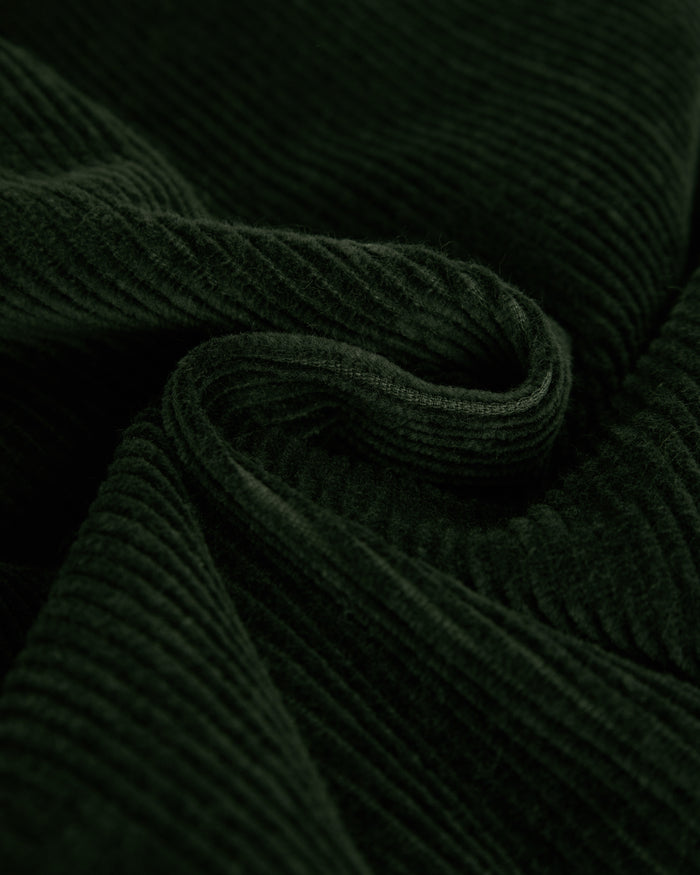 A close-up shot of the soft, ribbed fabric of The CÔTELÉ Corduroy Straight Pants in forest green, highlighting the textured mid-wale corduroy material.