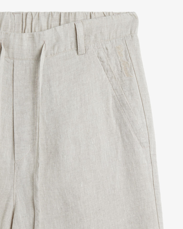 The Holiday Linen Trouser in natural — close-up of the waistband and embroidered logo