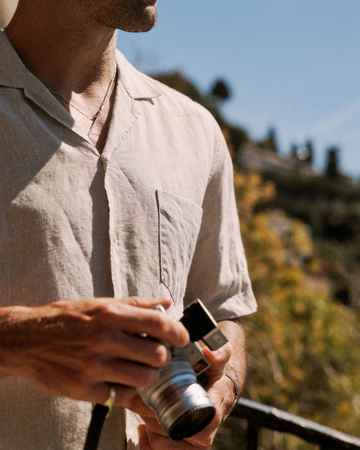 The Holiday Linen SS Shirt in natural — worn while holding a vintage camera
