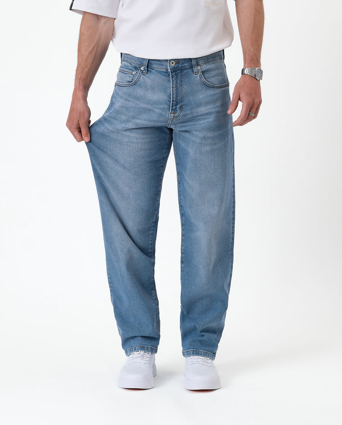 The Jeans Relaxed Straight Fit in Light Midwash — pulling the leg to show the stretch fabric