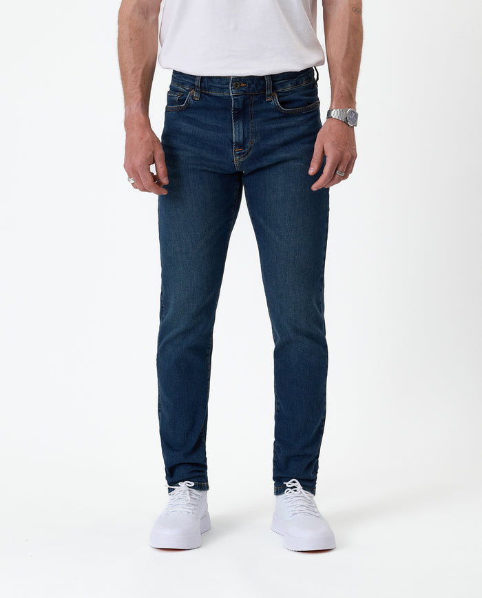 The Jeans Skinny Fit in Midwash — front view worn with white sneakers