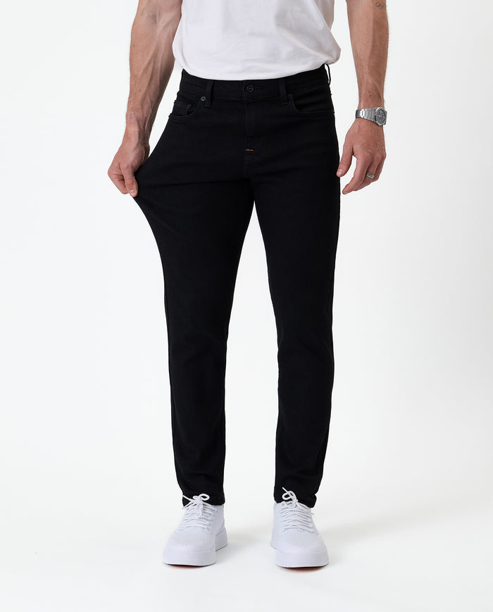 The Jeans Skinny Fit in jet black — pulling at the thigh to show the fabric's stretch