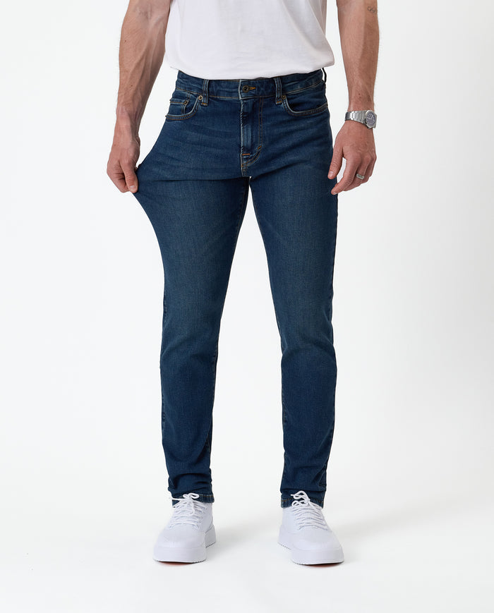 The Jeans Skinny Fit in midwash — fabric being pulled to demonstrate stretch
