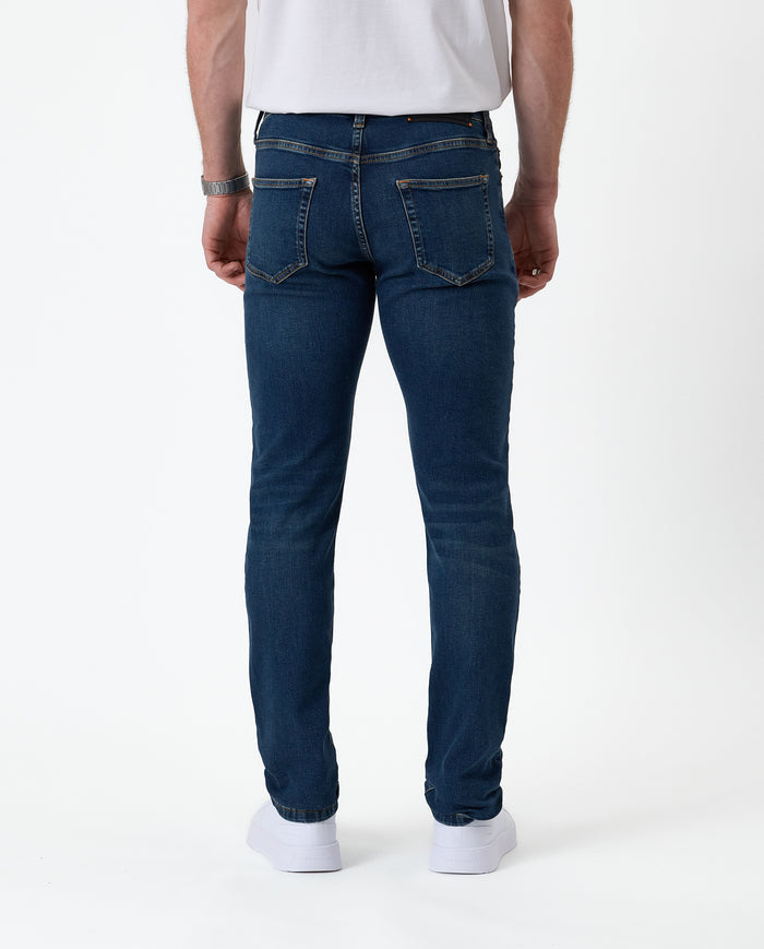 The Jeans Skinny Fit in midwash — back view worn with white sneakers