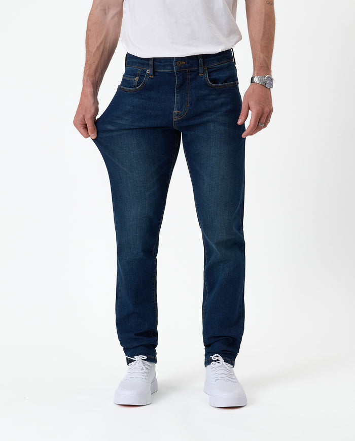 The Jeans Slim Fit in Midwash — model pulling the fabric to demonstrate stretch