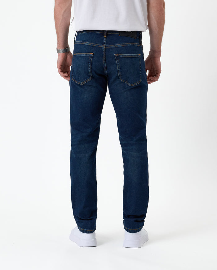 The Jeans Slim Fit in midwash — back view with the C'est normal rubber patch